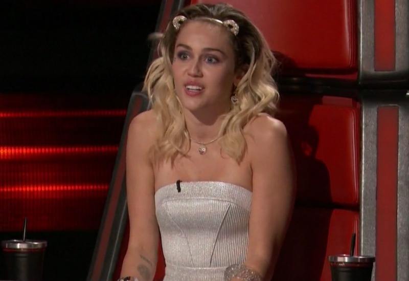 Miley Cyrus sits in a coach's chair on The Voice