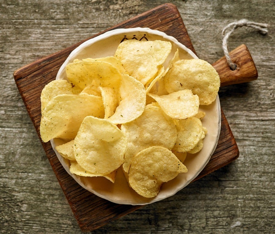 Bowl filled with potato chips sitting on wooden table.