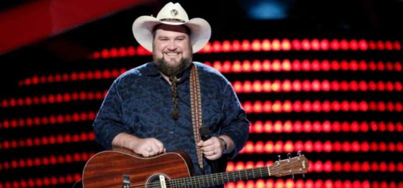 Sundance Head is holding is guitar and smiling on the stage of The Voice.