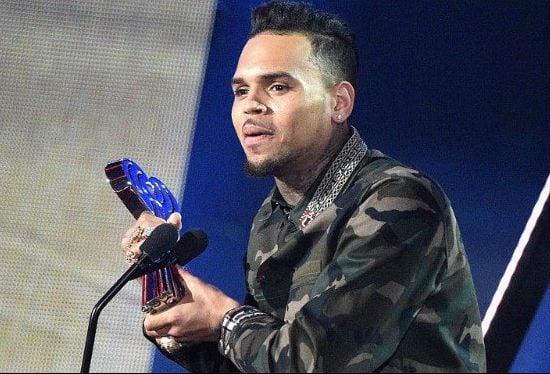 Chris Brown speaking into a microphone, wearing a black leather jacket