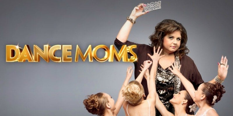 Abby Lee Miller holds a crown in the air as little girls try to reach for it on Dance Moms.