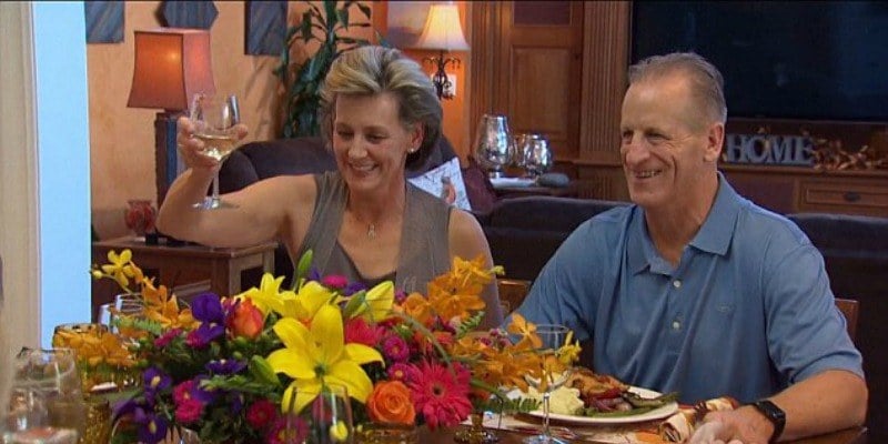 Jordan Rodgers' parents sit in front of dinner plates and hold up a glass of wine