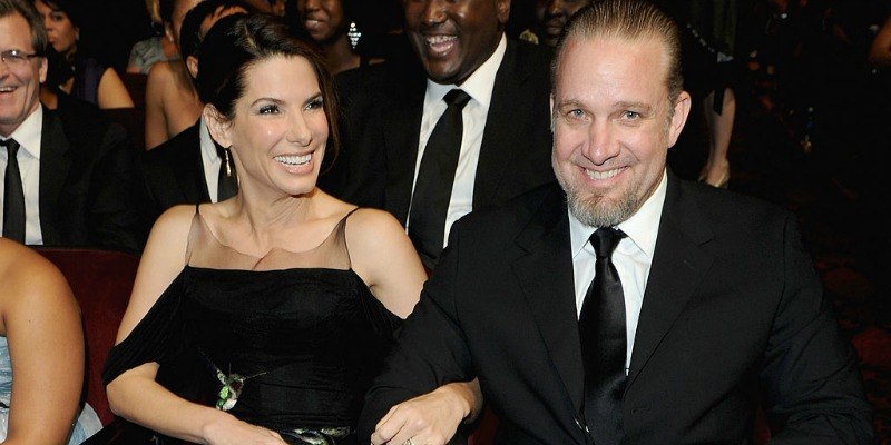 Sandra Bullock and Jesse James are sitting down in an audience smiling.