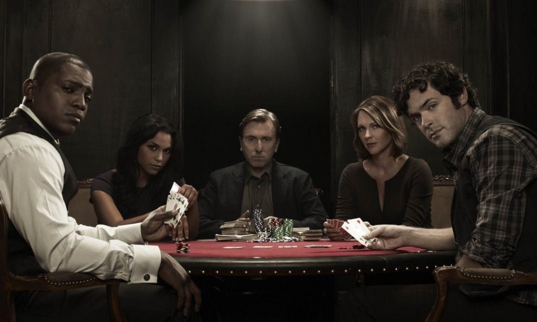 The cast of Lie to Me sits around a poker table looking at the camera