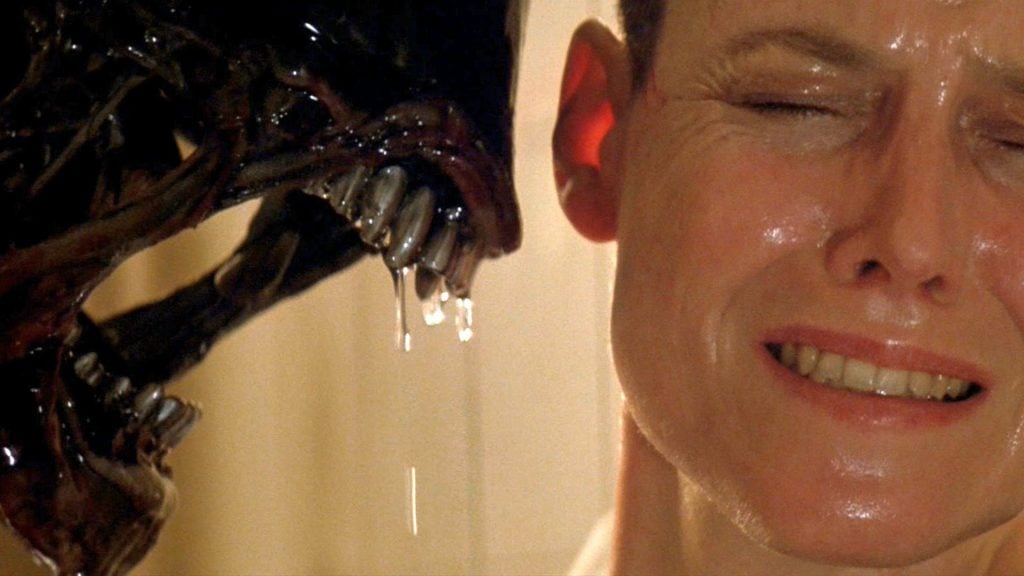 A Xenomorph roars at Ripley, who has her eyes closed and her teeth bared
