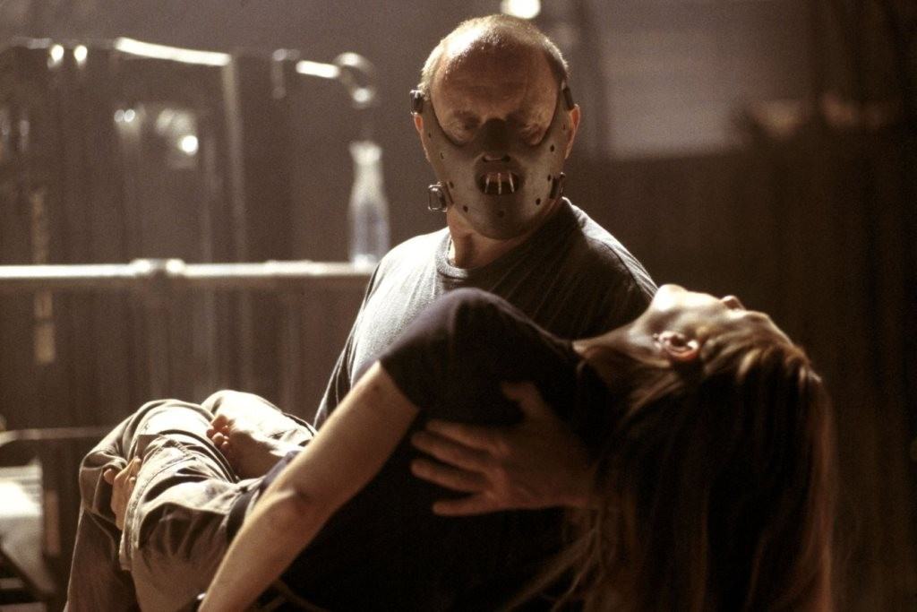 Hannibal holds an unconscious woman in his arms, wearing his trademark mask
