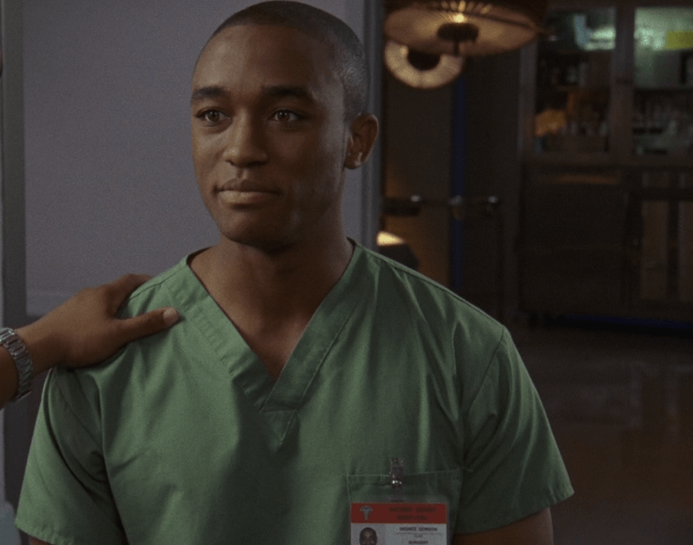 Lee Thompson young wearing surgeons scrubs with a hand on his shoulder