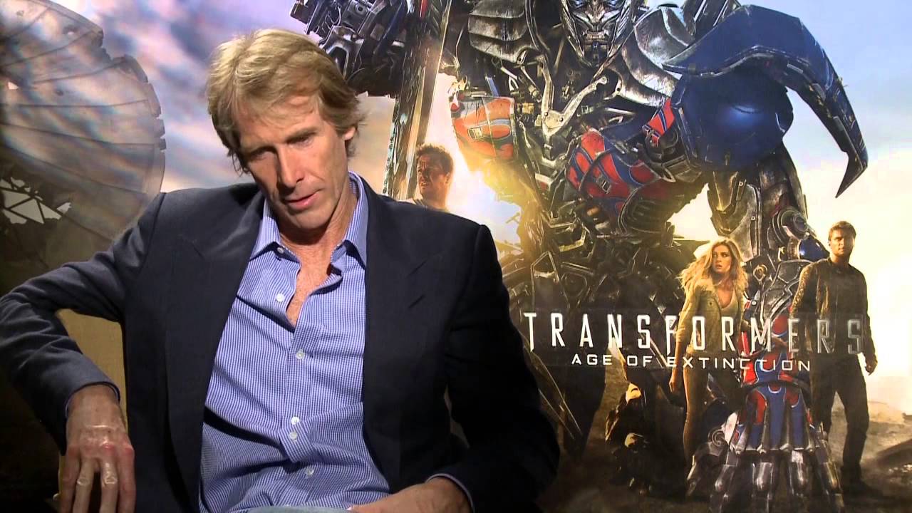 Michael Bay in an interview, sitting in front of a Transformers poster background