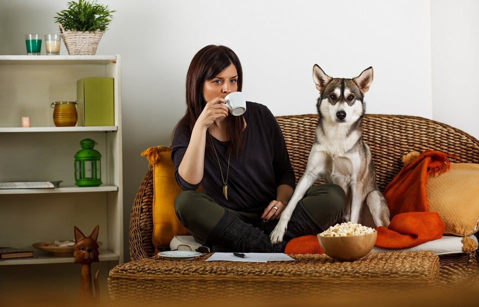 Young woman drinks her coffee on the couch alongside her dog