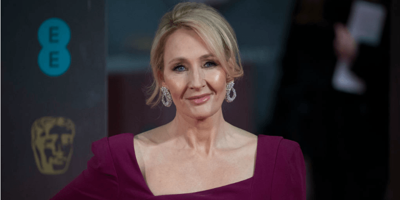 J.K. Rowling is in a purple dress smirking at the camera