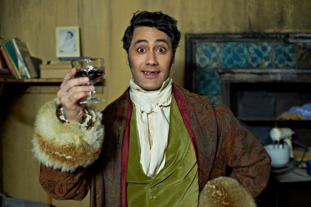 Taika Waititi smiling and holding a glass of wine in What We Do In the Shadows