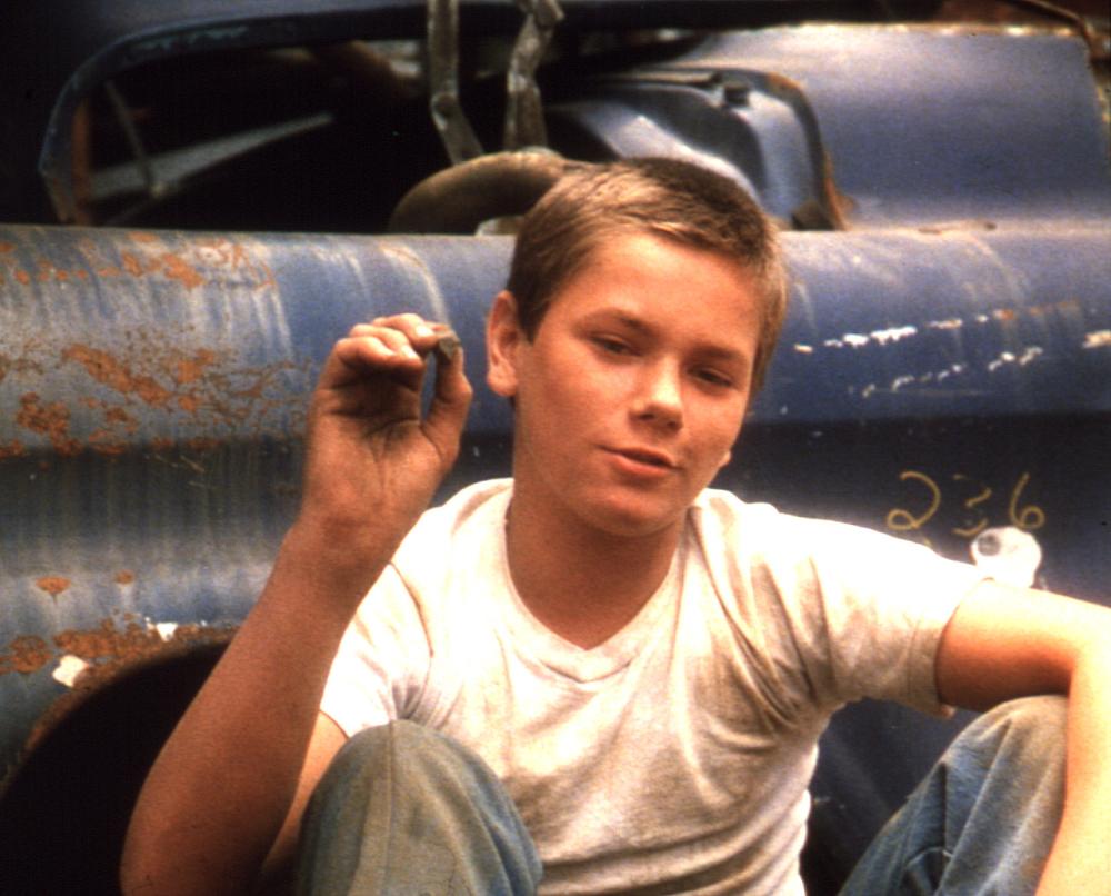 Young River Phoenix sits next to an old card in a white t-shirt in Stand by Me 
