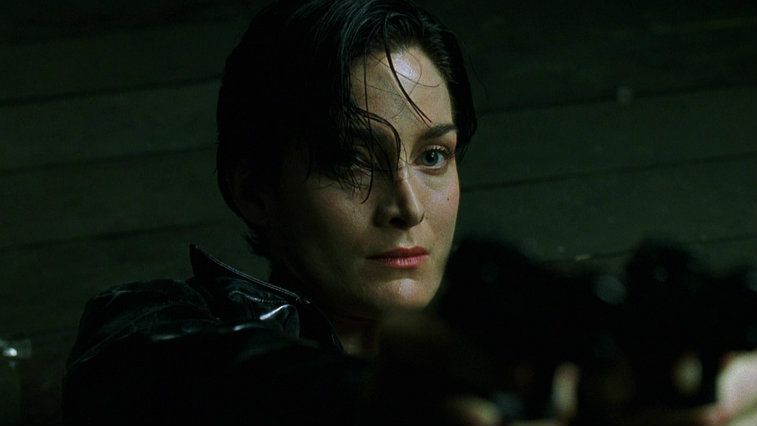 Carrie-Anne Moss looking into the camera in a dark room in The Matrix