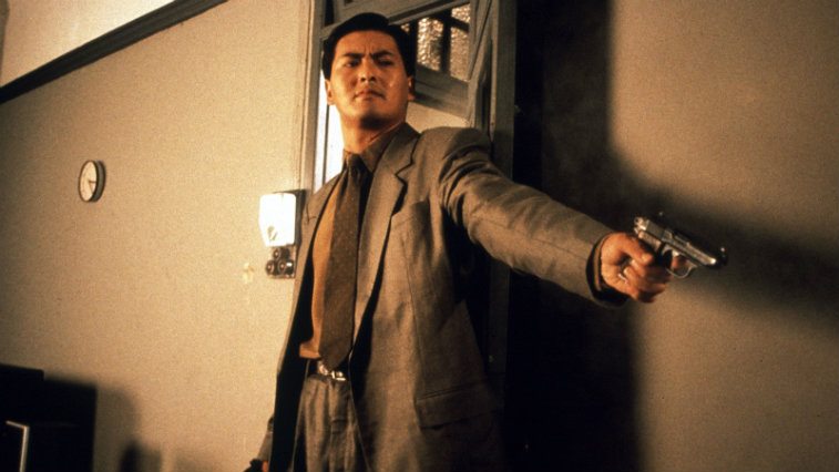 Chow Yun-Fat standing in a room pointing a gun in The Killer