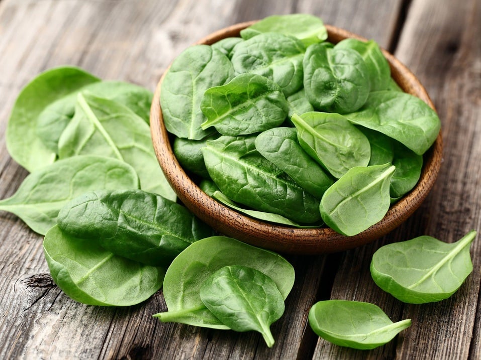 Spinach in and around a bowl on a wooden table.