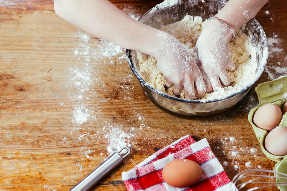 A woman's hands covered in flour kneading dough in a bowl in preparation for baking.