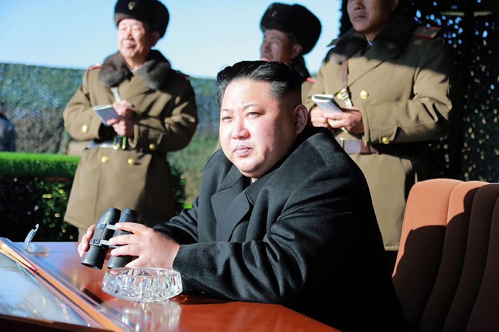 Kim Jong Un sits at a table holding binoculars