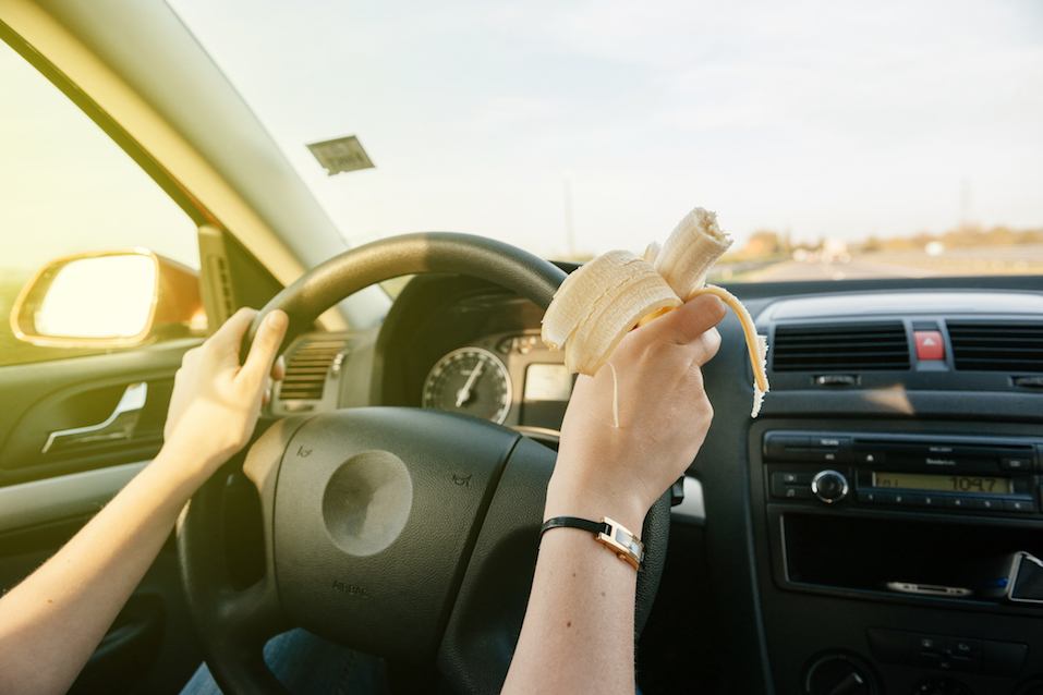 A woman eats a banana while driving.