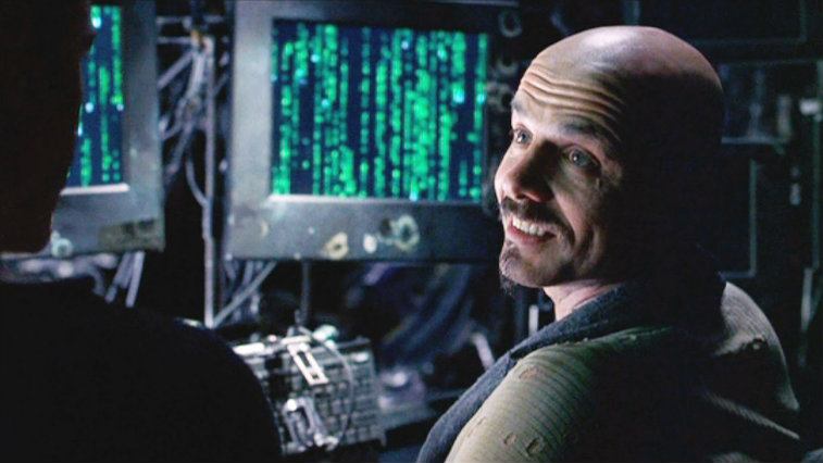 Joe Pantoliano looking over his shoulder and smiling in The Matrix