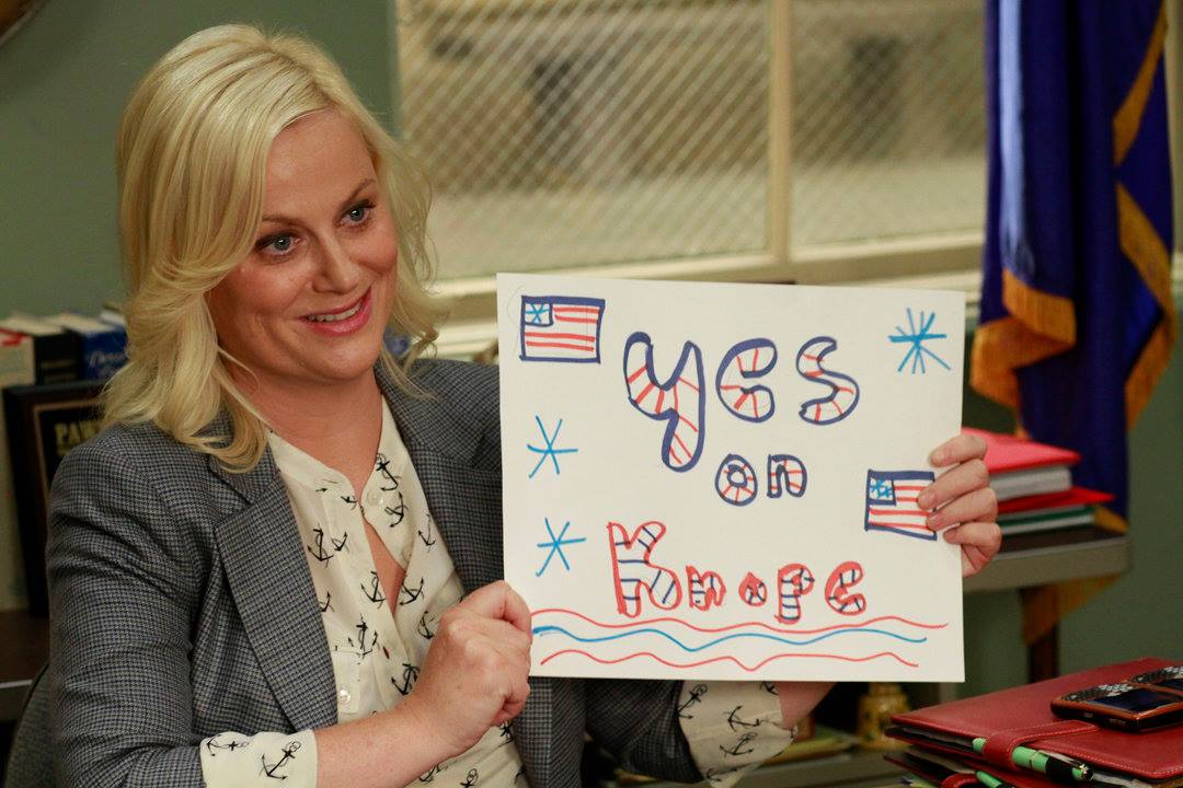 Leslie Knope holding up a sign that says "Yes on Knope"