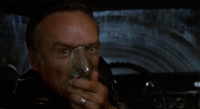 Frank Booth is in a car and turns around to the backseat and puts an oxygen mask on his face.