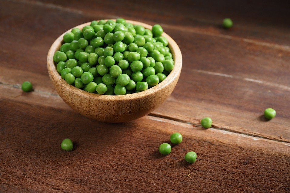 Fresh green peas in bowl on wooden background.
