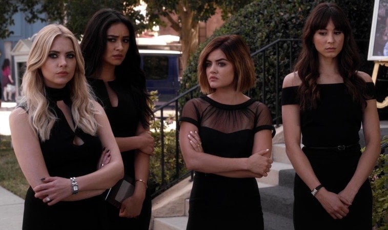 Four girls in black dresses stand outside next to steps looking concerned