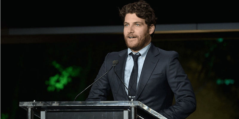 Adam Pally is talking on stage at a podium.
