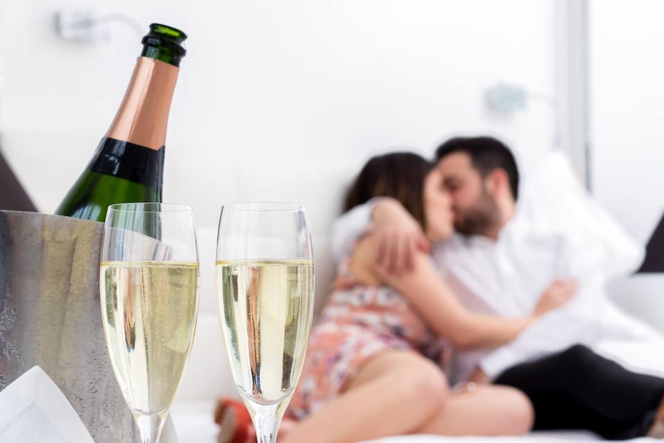 Champagne glasses and cold bottle in ice bucket with kissing couple in background