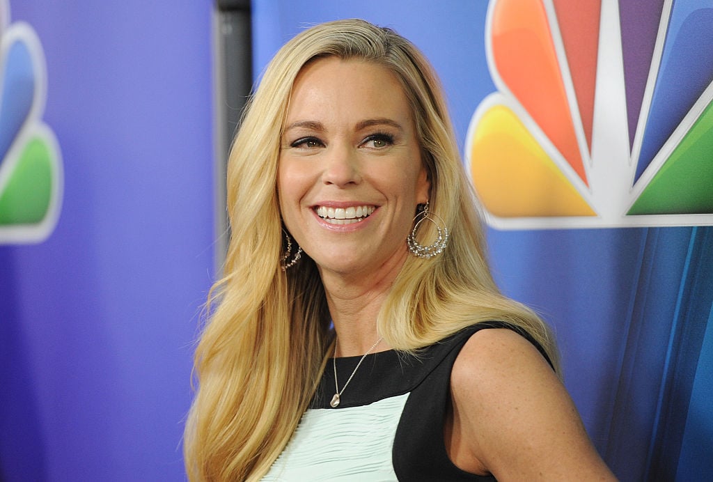 Kate Gosselin smiling, wearing a dress in front of an NBC logo 