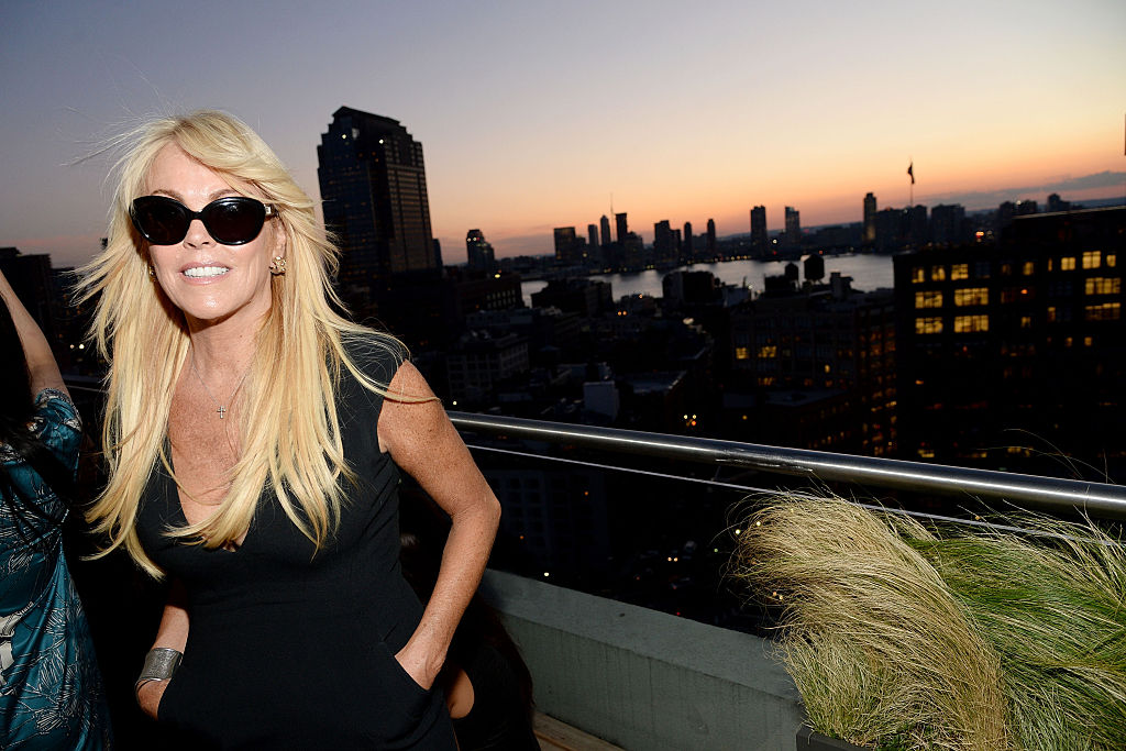 Dina Lohan smiling, in front of a sunset over a city skyline