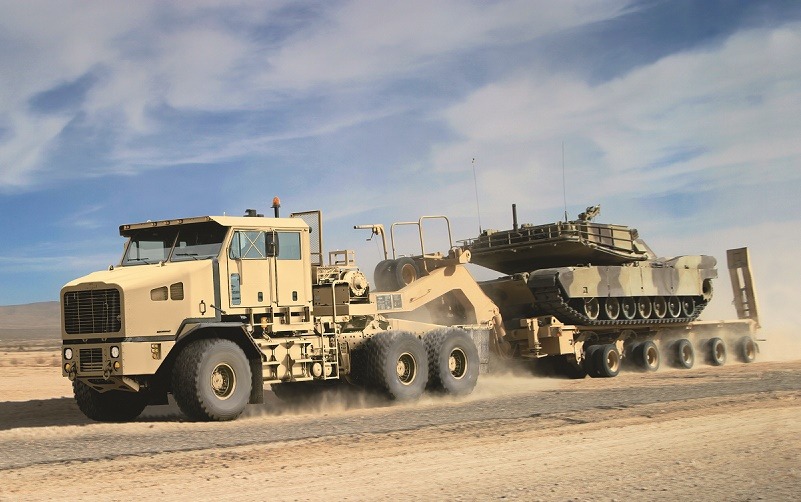 A Global Heavy Equipment Transporter towing a tank across the sand.