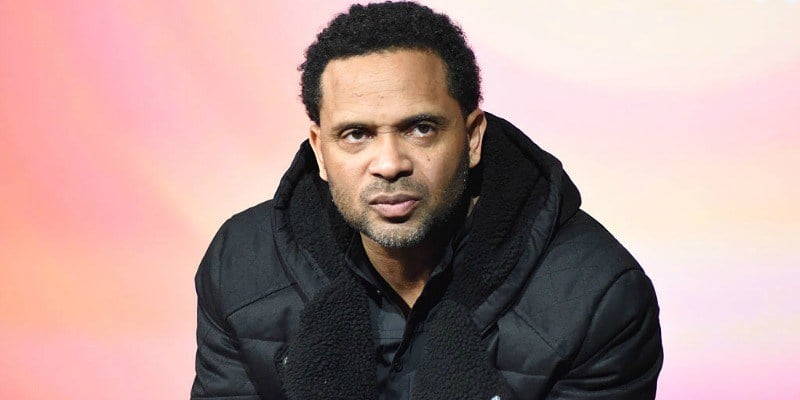 Mike Epps is in a black jacket and looks seriously ahead.