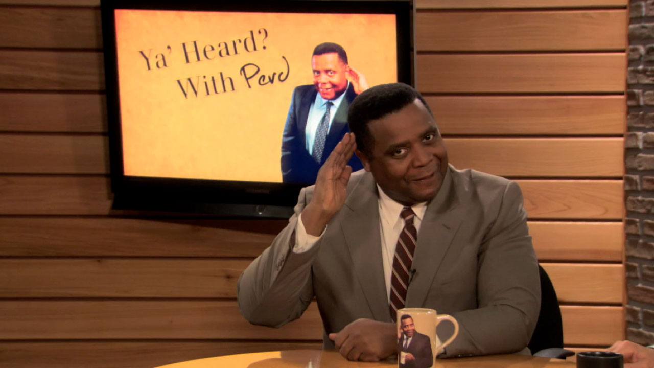 Perd Hapley saluting, sitting behind a news desk