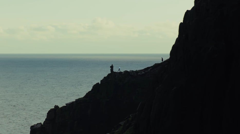 A long shot of Rey training with a lightsaber on a cliff face, while Luke patiently looks on