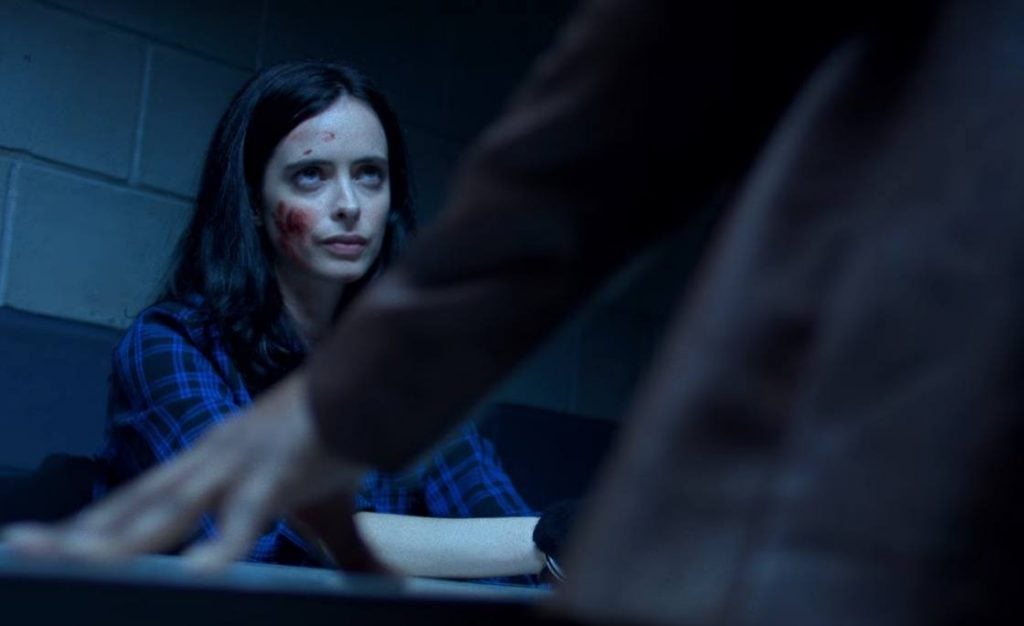 Jessica Jones scowling, sitting in an interrogation room