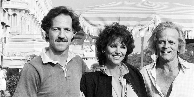 Werner Herzog, Claudia Cardinale, and Klaus Kinski have their arms around each other and are smiling.
