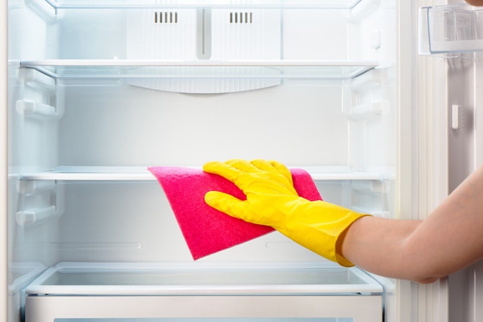 cleaning white open empty refrigerator with pink rag