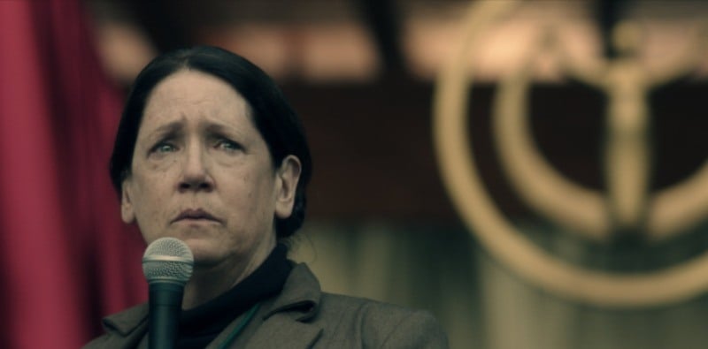 Aunt Lydia is on stage in front of a microphone with tears in her eyes.