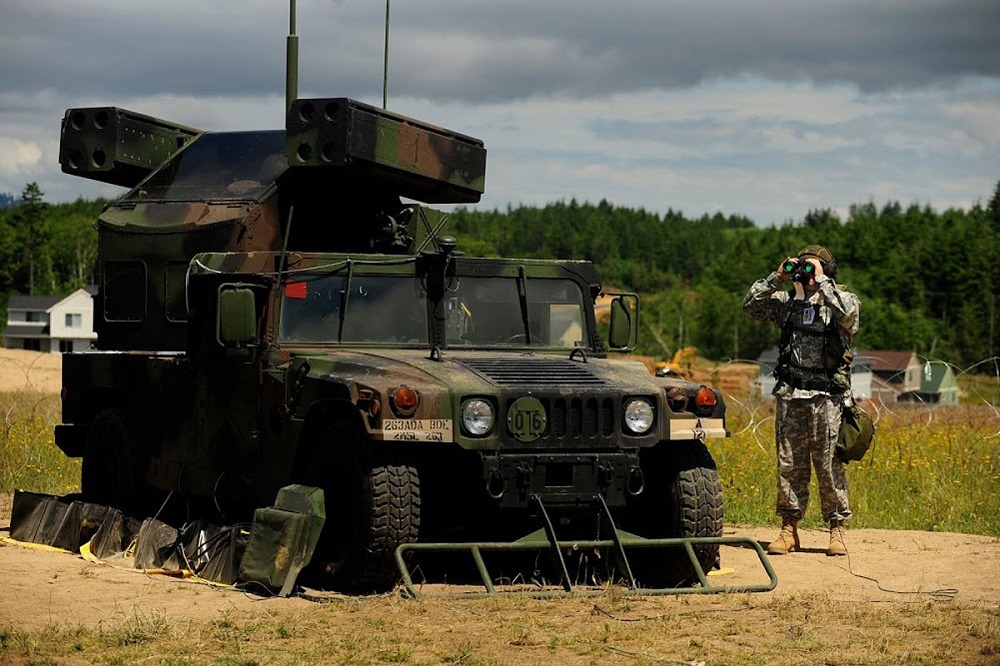 A camouflage painted Avenger Weapon System parked in a field.