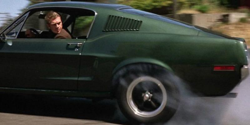 Steve McQueen is speeding away in a mustang and looking back out of the window.