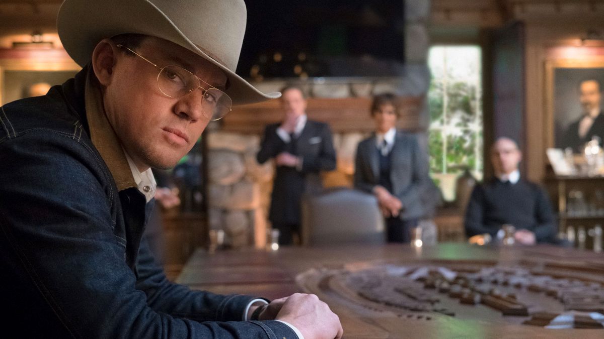 Channing Tatum wearing a cowboy hat while sitting at a table, turning to look into the camera