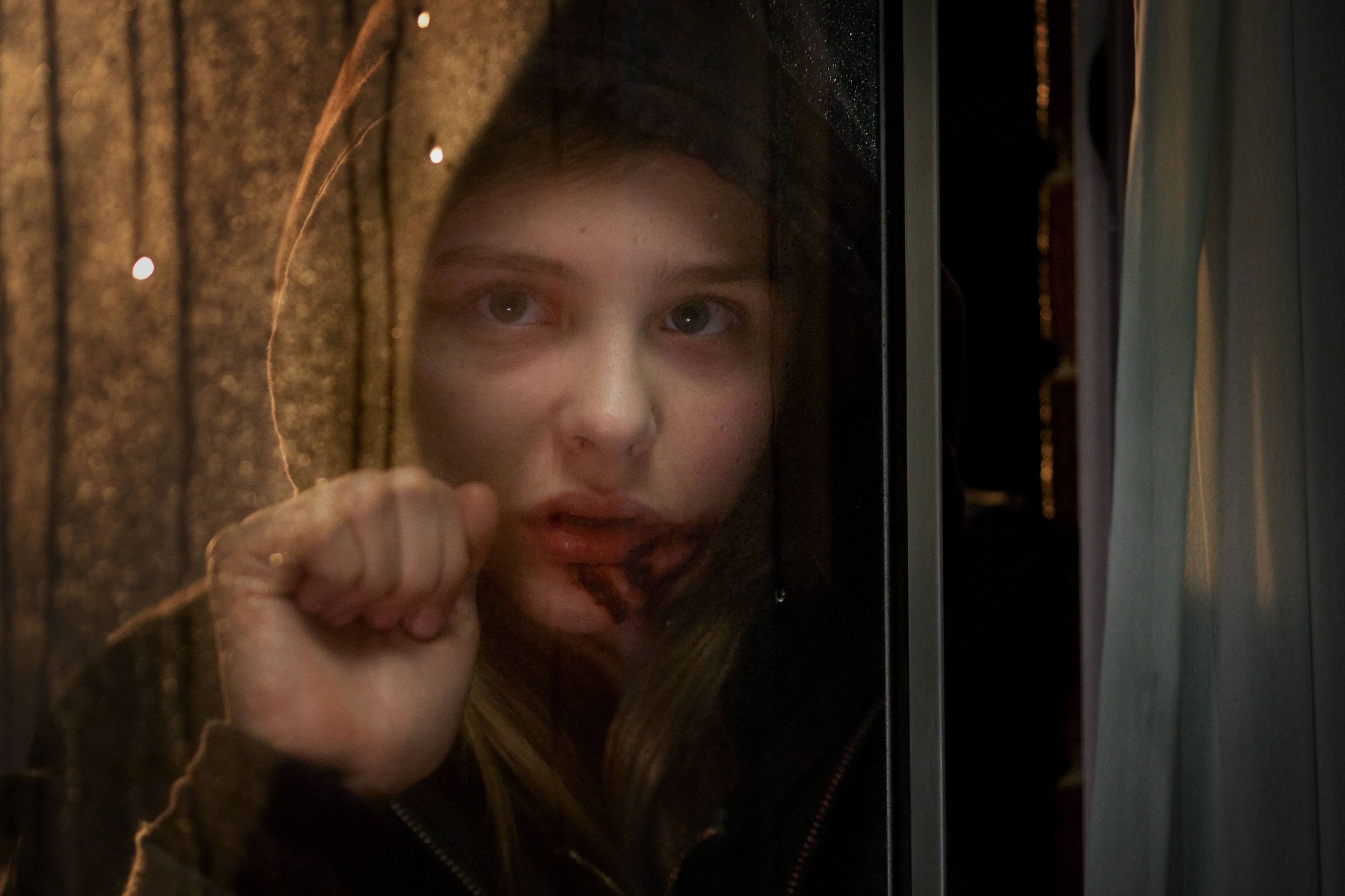 Abby wears a hood and knocks on a window in a scene from 'Let Me In.'