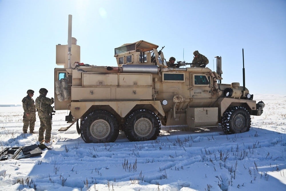 Soldiers stand outside a Cougar 6x6 MRAP in a snowy field.
