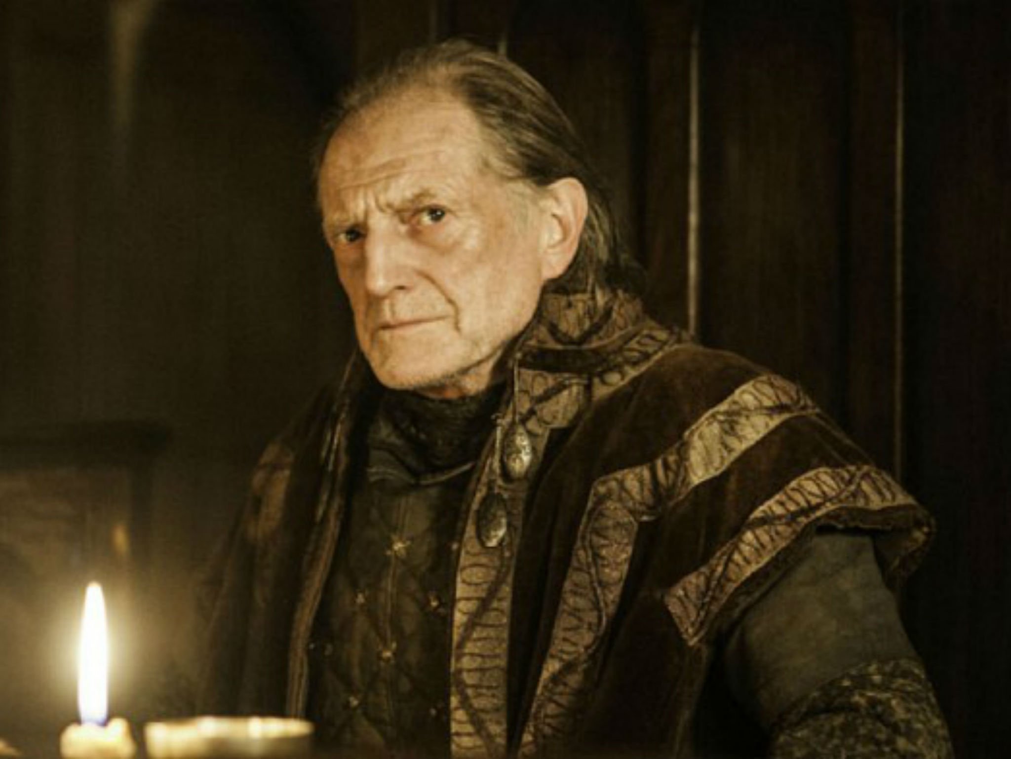 Walder Frey sits at a table, a lit candle in front of him, in a scene from 'Game of Thrones.'
