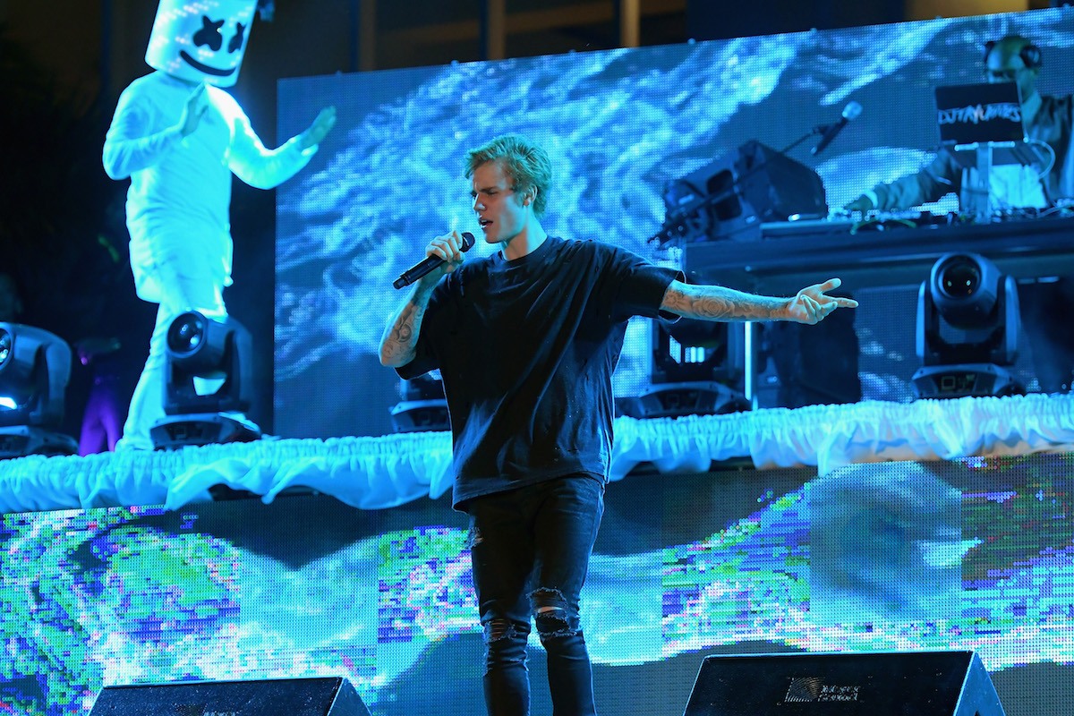 Justin Bieber, wearing all black, sings into a microphone as he gestures with his left hand during a performance.