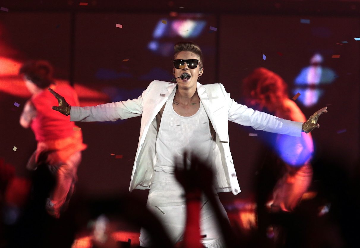 Justin Bieber, wearing an all-white suit, black sunglasses and gloves, sings on stage. 