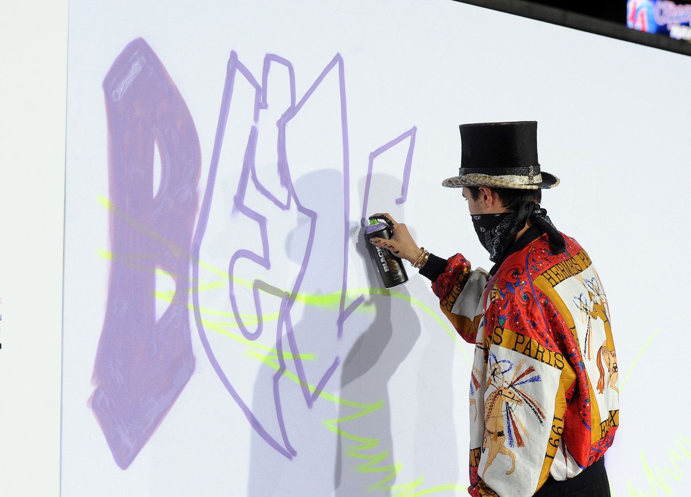 Justin Bieber spray paints the word 'Believe' onto a white wall.