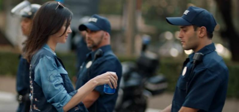 Kendall Jenner is handing a police man a Pepsi.