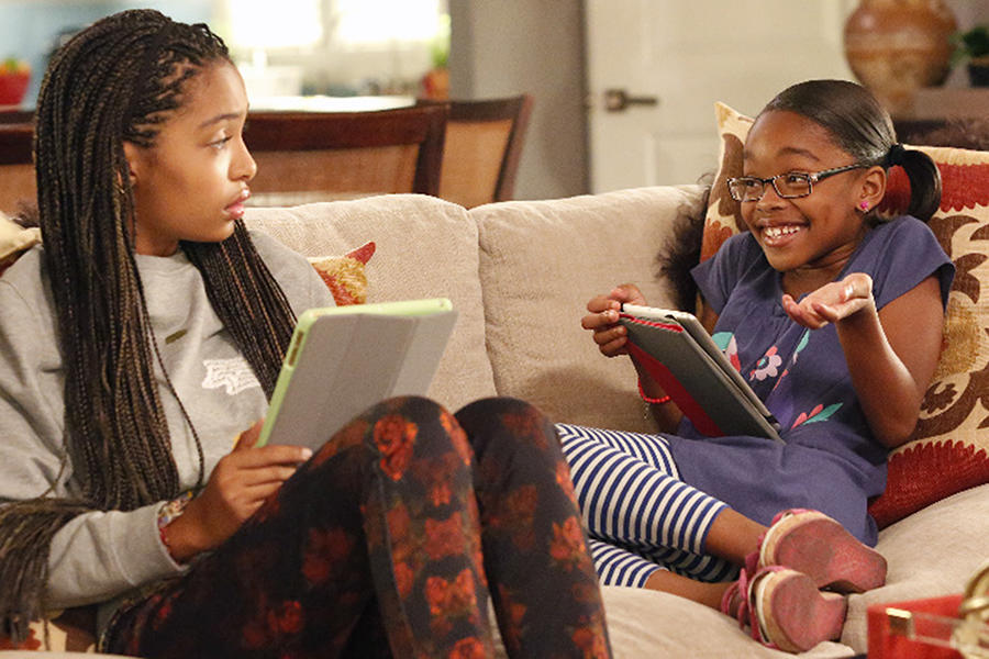 Zoey looks at Diane, who shrugs while smiling, as they both hold tablets and sit on a couch in a scene from the ABC comedy 'Black-ish.'